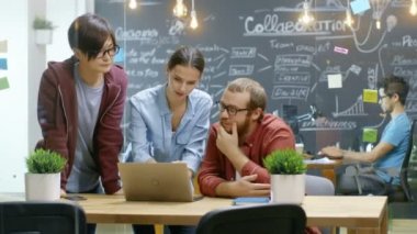 Üç yaratıcı insanlar Laptop kullanırken Active devam eden proje hakkında tartıştık. Modaya uygun ortamda iş şık gençler.
