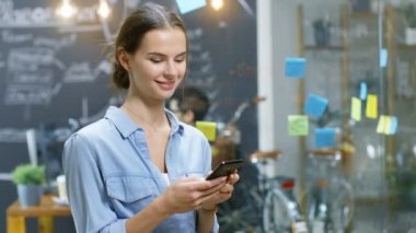 Genç kadın büyüleyici Smartphone, gülümser güzel fotoğraf makinesinde meşgul yaratıcı Office şık yetenekli insanlarla ayakta iken kullanır.