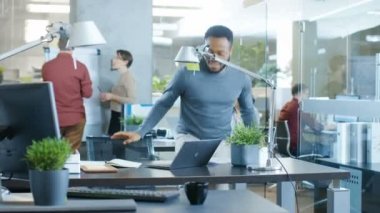Uluslararası Ofis, Afrikalı-Amerikalı adam onun defter hatırlatmak içinde yazdığı bir dizüstü bilgisayarda onun masasında çalışma meşgul. Arka planda çalışan yaratıcı gençler.