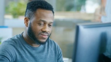 Bir kişisel bilgisayar üzerinde genç siyah adam çalışır tatlı kamerada gülümsüyor. Kesilmiş sakallı şık akıllı adam.