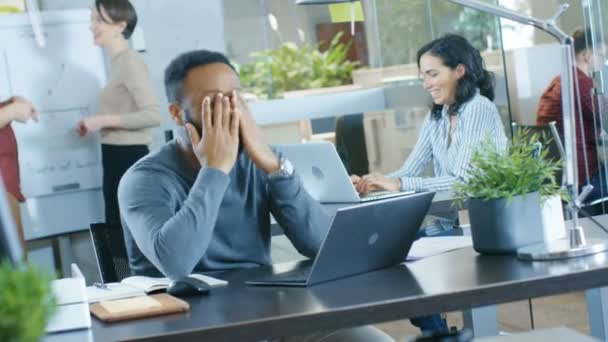 黑衣人在办公桌上工作的笔记本电脑 遇到滑稽的错误和笑 在背景创意年轻人做他们的工作 现代明亮的办公室 — 图库视频影像