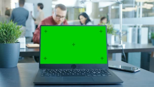 テーブルの上の緑のモックアップ画面のノート パソコン モダンなオフィスで働く若い創造的な専門家の背景で — ストック動画