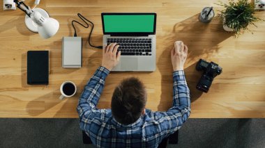 Onun Laptop ile yeşil ekranda üstten görünüm genç fotoğrafçı işleme fotoğrafları. Kamera, dış sabit disk ve defter onun yanında yalan.