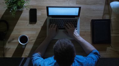 Üstten Görünüm geceleri onun laptop yaratıcı tasarımcı çalışma. Masasına soğuk mavi ışık--dan dış tarafından aydınlatılmış.