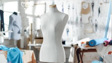 Bir kadeh bir terzilik manken bir parlak ve güneşli Studio duruyor. Çeşitli dikiş öğeleri ve renkli kumaşlar etrafında döşeme, ayakta mankenler ve skeçler duvara sabitlenmiş.