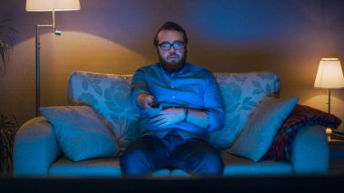 Bir adam onun oturma odasında kanepede oturan, Tv izlerken, kanal değiştirme portre vurdu. Zemin lambaları döndü yanıyor.