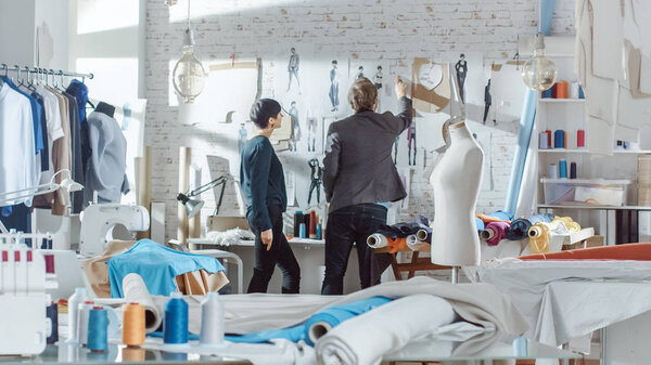 Женская и мужская мода, дизайнер, модельер и приклеивающаяся к стене одежда - эскизы к их новой коллекции. Студия это Санни. Цветные ткани, вешание одежды и пошив предметов видимы
.