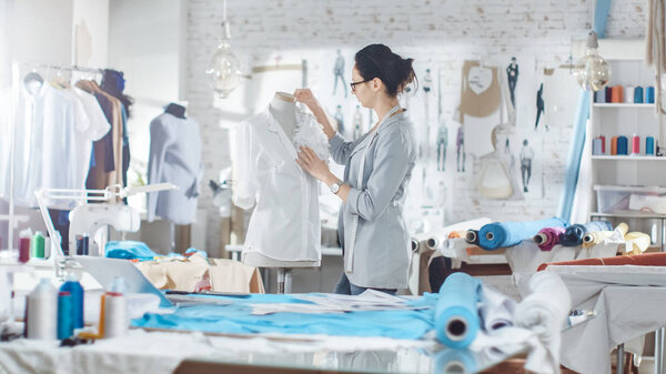 Beautiful Woman fashion, designer,  Working with Tailoring Mannequin, Adjusting Blouse. Her Studio is Bright and Sunny, Mannequins Standing around, Clothes Hanging, Colorful Fabrics Lying on the Table.