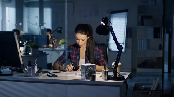 Beautiful Female Design Engineer Working on Drafts Late at Night. Her Office is Empty, Blue City Light Shines Through Windows.