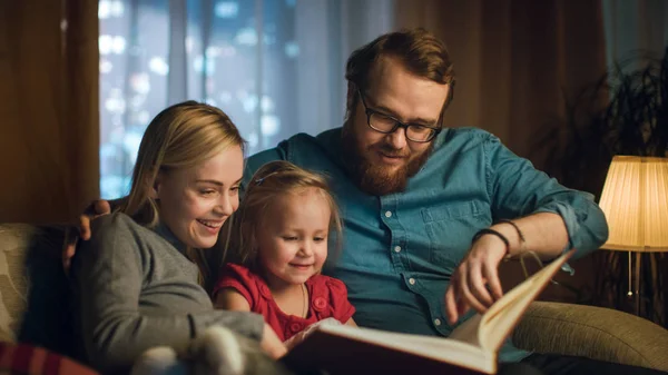 Isä Äiti Pieni Tytär Lukemassa Lastenkirjaa Sohvalla Olohuoneessa Iltaa — kuvapankkivalokuva