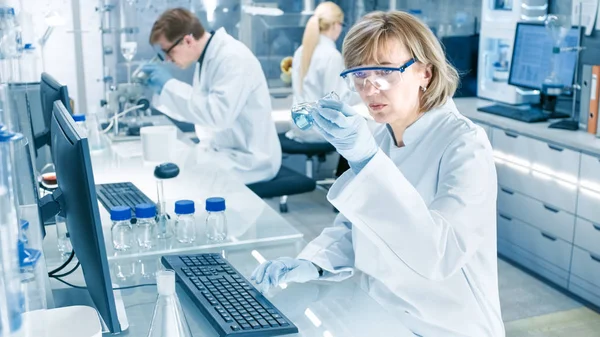 女性科学者は 彼女のコンピューター上観測をビーカーなどの液体を分析します 彼女は忙しい研究室で働いている科学者の実験の完全な — ストック写真