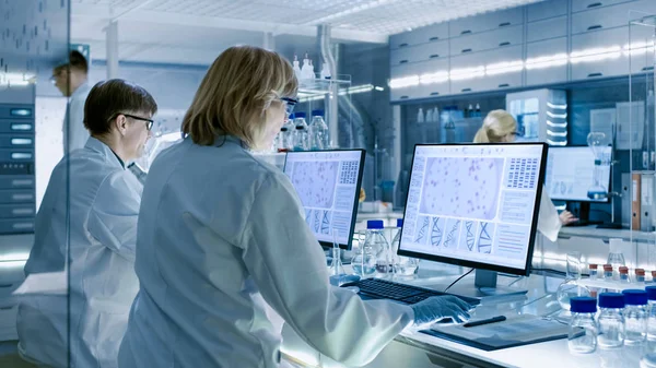 女性と男性の科学者実験に取り組んでそのコンピューターで大きなモダンな ビーカー 化学物質別の技術的な機器と様々 な棚が表示 — ストック写真
