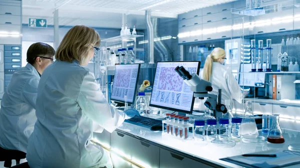 女性と男性の科学者実験に取り組んでそのコンピューターで大きなモダンな ビーカー 化学物質別の技術的な機器と様々 な棚が表示 — ストック写真