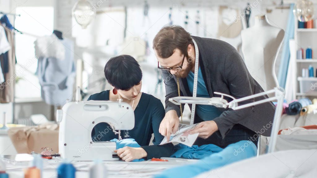 Male and Female fashion, designer, s are Working on Tailored Mannequin Wearing Clothes. They Also Use smartphone. In Their Studio Sewing Machine, Fabrics and Sketches are Visible.