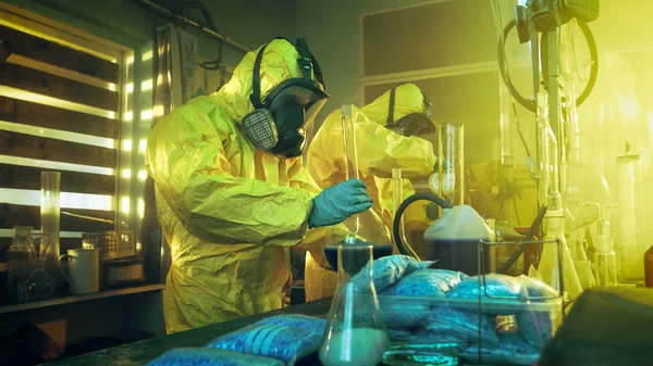 地下の研究室で保護つなぎ服およびマスクを身に着けている つの秘蜜化学は薬を調理します ビーカー 蒸留ガラス 缶とホースが使用します 真の犯罪概念 — ストック写真