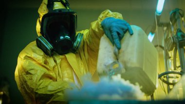 In the Underground Drug Laboratory Clandestine Chemist Wearing Protective Mask and Coverall Mixes Chemicals. He Pours Liquid From Canister into Bowl, Toxic Compounds Create Smoke. He Works in the Abandoned Building.