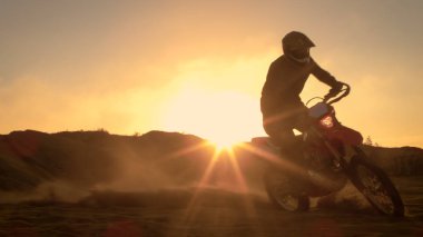 Profesyonel motokros motosiklet binici Off-Road kum arazi üzerinde kullanıyor. Günbatımı ve şarkı duman, sis ve puslu güneş ışığı ile kaplı olmasıdır.