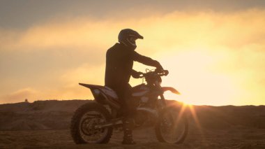 Fmx motosiklet binici Onun Bisiklet ve bakan zor Sandy Off-Road arazi üzerinde duruyor. Güneş batıyor.