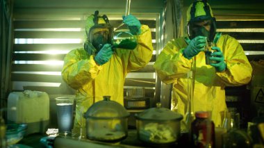 In the Underground Drug Laboratory Two Clandestine Chemists Wearing Protective Masks and Coveralls Test Cooked Drug's Purity and Strength. They Work in the Abandoned Building Full of Glassware and Cooking Equipment. clipart