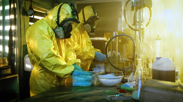 地下の研究室で防護マスク つなぎ服を着て つの秘蜜化学のバッグパック合成水晶 Meth のボックスにさらに配布 研究室はフルの違法な装備です 彼らは断念された建物にスクワットします — ストック写真