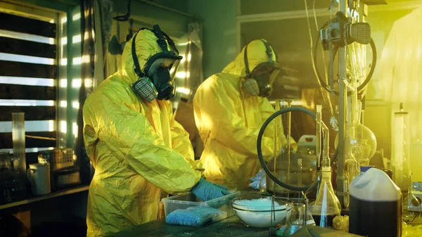 地下の研究室で防護マスク つなぎ服を着て つの秘蜜化学のバッグパック合成水晶 Meth のボックスにさらに配布 研究室はフルの違法な装備です 彼らは断念された建物にスクワットします — ストック写真