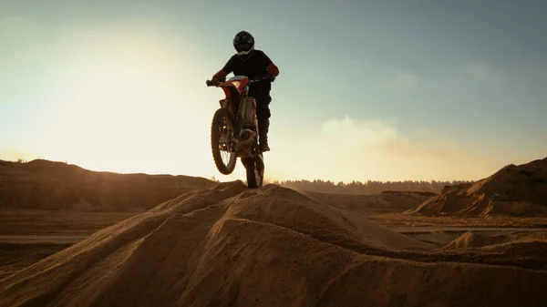 专业摩托车越野摩托车骑手在沙丘上行驶和进一步下跌的越野的轨道 它是日落和轨道上布满烟雾 — 图库照片