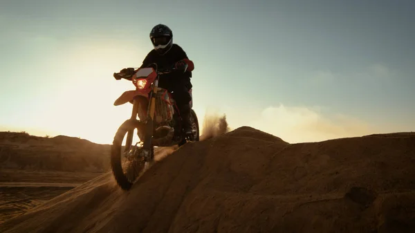 Professional Motocross Motorcycle Rider Driving Over the Dune and Further Down the Off-Road Track. It\'s Sunset and Track is Covered with Smoke/ Mist.