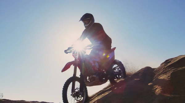 Low Angle Footage of the Professional Motocross Motorcycle Rider Drives off the Dune and Down the Terrain.