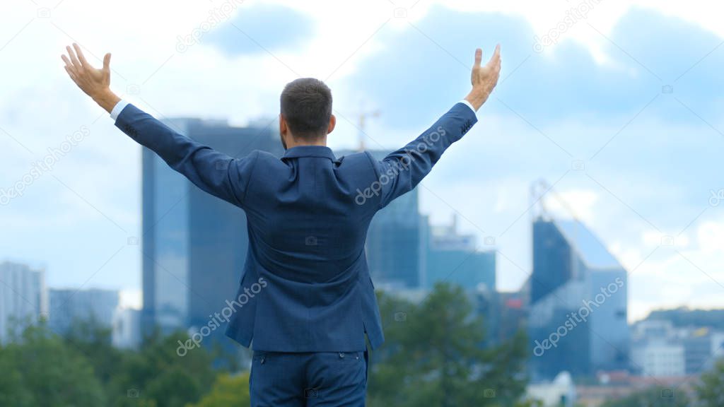 Happy Successful Business Man Raises His Hands, He Has His Business Victory. In The Background Big City with Skyscrapers.