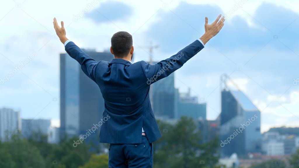 Happy Successful Business Man Raises His Hands, He Has His Business Victory. In The Background Big City with Skyscrapers.