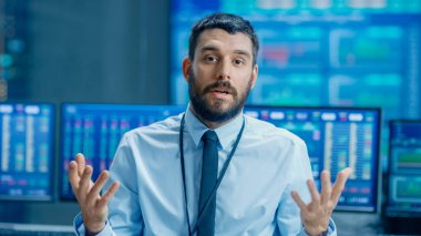 Profesyonel borsa tüccar Charismatically kameraya konuşuyor. Arkasından Ticker sayılar, veriler, grafikler ile bilgisayar ekranları.