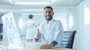 Fütüristik laboratuvarda erkek bilim adamları gösterilen sinyal başparmak. Şeffaf ekran bilgisayar üzerinde çalışıyor. Etkileşimli Dna görüntüleme, istatistiksel veri ve fütüristik Kullanıcı arabirimi ekran gösterir.