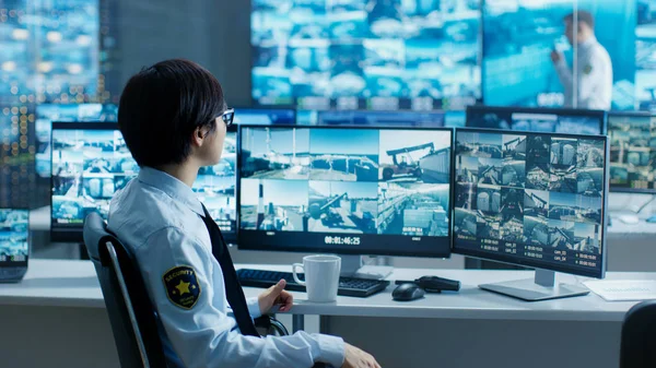 In the Security Control Room Officer Monitors Multiple Screens for Suspicious Activities, He Drinks from a Mug. He\'s Surrounded by Monitors and Guards Port of National Importance.