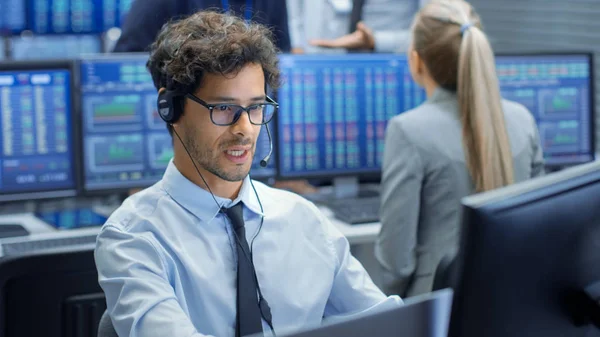 Stock Trader Making Sales with a Headset. In the Background Stock Exchange Office and Group of Traders Working at their Workstations.