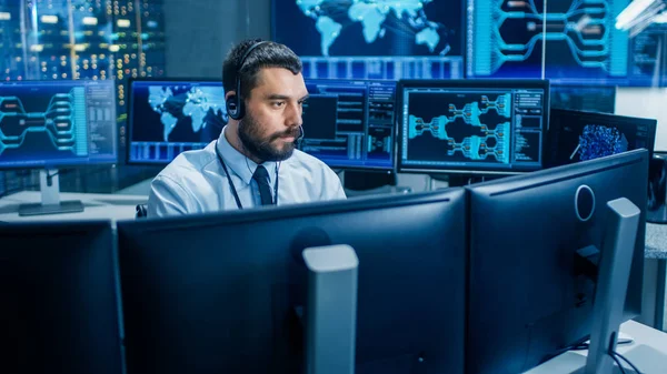In the System Monitoring Room Dispatcher Wearing Headset Observers Proper Functioning of the Facility. He\'s Surrounded by Screen Showing Technical Data.