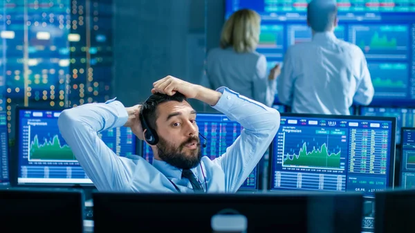 Stock Exchange Trader Makes a Deal with Big Client Over the Headset. He Works with Other Brokers and is Surround By Computers with Graphs and Ticker Numbers on Screens.