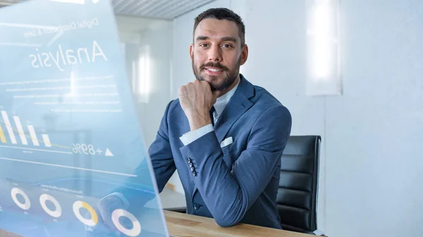 In the Near Future Successful Businessman Works on Computer with Transparent Display that Shows Stock Market Analyzing Data, Pie Charts, Rises and Downs.