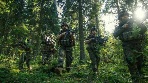 Squad of Five Fully Equipped Soldiers in Camouflage on a Reconnaissance Military Mission, Rifles Ready. They're Moving in Formation Through Dense Forest. Low Angle Footage.