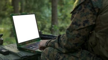 Yakın çekim asker kullanır askeri sınıf Laptop ile beyaz/yeşil perde. Askeri üste ormanın içinde arka planda kamufle.