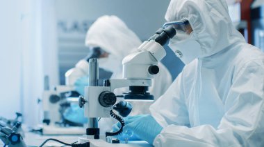 İki mühendis / bilim adamları / teknisyenleri steril temiz oda takım elbiseli kullanın mikroskoplar bileşen ayarı ve araştırma için. Onlar bir elektron komponentler fabrika üretim iş.