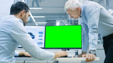 Endüstriyel tasarımcı Cad programında çalışırken Kıdemli mühendis ile konuşma, bir yeşil ekran Chroma anahtar şablon büyük Mockup için vardır. O inşaat üstünde kişisel bilgisayar ile iki monitör.