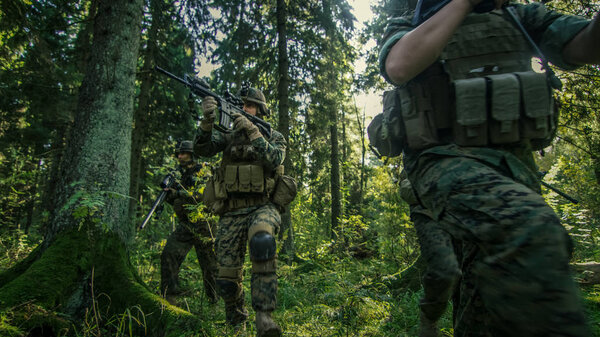 Squad of Fully Equipped Soldiers in Camouflage on a Reconnaissance Military Mission, Rifles Ready. They're Moving in Formation Through Dense Forest. Low Angle Footage.