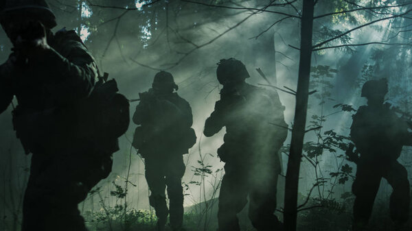 Squad of Five Fully Equipped Soldiers in Camouflage on a Reconnaissance Military Mission, Rifles Ready to Shoot. They're Moving in Formation Through Dense Smokey Forest.