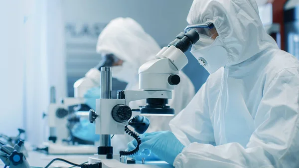 つのエンジニア 科学者 技術者無菌クリーン ルームのスーツにはコンポーネントの調整 研究顕微鏡を使用します 彼らは 電子部品製造工場で働く — ストック写真