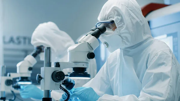 つのエンジニア 科学者 技術者無菌クリーン ルームのスーツに製造機械作業を制御し コンポーネントの調整 研究に顕微鏡を活用します 彼らは 電子部品製造工場で働く — ストック写真