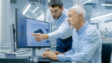 Endüstriyel tasarımcı konuşma Kıdemli mühendis ile yeni bileşen tasarımı Cad programında çalışırken vardır. O inşaat üstünde kişisel bilgisayar ile iki monitör.