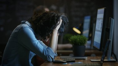 Yorgun, Overworked kadın cep telefonu App Tasarımcısı tutar onu kafasından bir kişisel bilgisayarda çalışırken elleri. Arka plan yaratıcı ofiste.