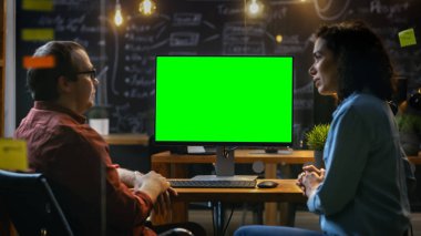 Güzel kadın ofis çalışanı onun resepsiyon müzakerelerinde erkek onun iş arkadaşınız ile masa üzerinde duran Mock-up bilgisayarla yeşil ekran. Yaratıcı akşam Office.