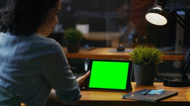 Genç kadın oturur onun ahşap masa Mock-up yeşil ile Tablet bilgisayarı kullanan ekran, o kullanır çeşitli çalmak ve dokunmatik jestleri.