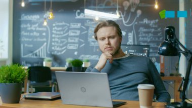 Yakışıklı genç Office çalışan düşünüyor bir dizüstü bilgisayarda çalışırken bir sorun çözüm üzerinde. Yaratıcı şık ofisinde çalışıyor.